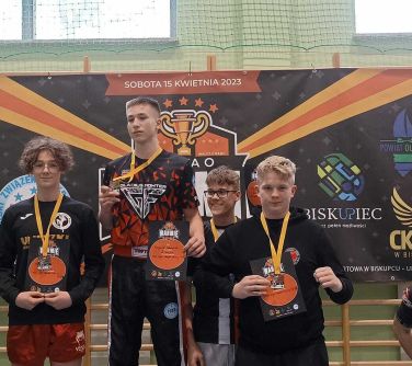 czterech nastolatków pozuje na podium, w tle baner obok mężczyzna