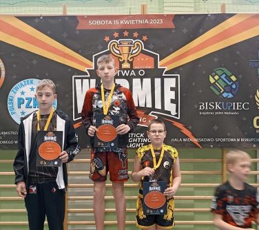 trójka dzieci pozuje do zdjęcia na stojąc na podium, w tle baner