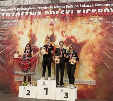 cztery osoby pozują na podium, w tle baner