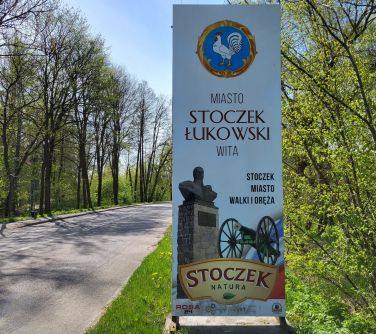 zdjęcie tablicy witającej Miasto Stoczek Łukowski wita, ulica po obu stronach drzewa