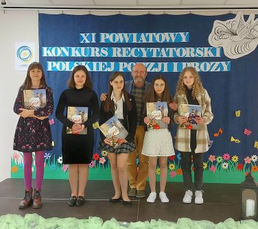 osoby stoją na scenie, w tle granatowa płachta z tytułem głównym XI Konkurs Recytatorski Polskiej Poezji i Prozy, na dole...