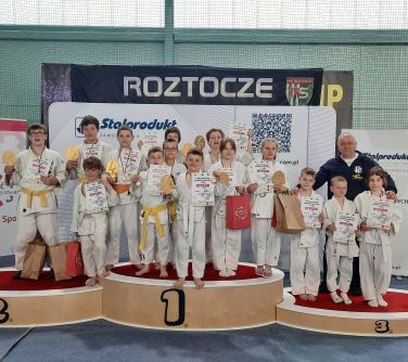 dzieci z trenerempozują do zdjęcia stojąc na podium, w tle baner