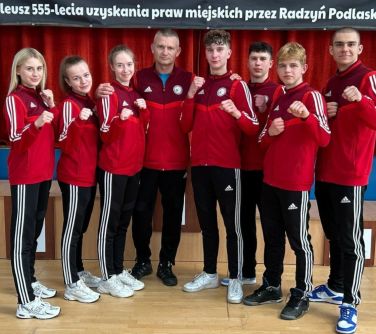 grupa zawodników taekwon-do w czerwonych bluzach pozuje do zdjęcia z trenerem