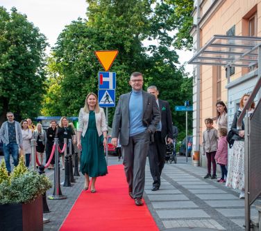 mężczyzna idzie po czerwonym dywanie, za nim osoby, obok osoby obserwujące