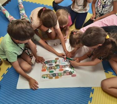 grupa dzieci pochyla się nad dużą kartką papieru siedząc na piankowych matach