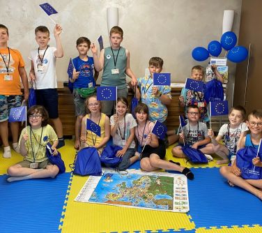 grupa dzieci pozuje do zdjęcia trzymając w dłoniach małe flagi ue