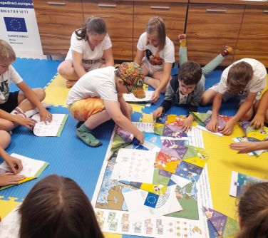 dzieci siedza na piankowych matach składają origami