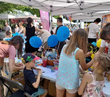 osoby z dzićmi wykonują rysunki przy stole, na stole balony, gadżety