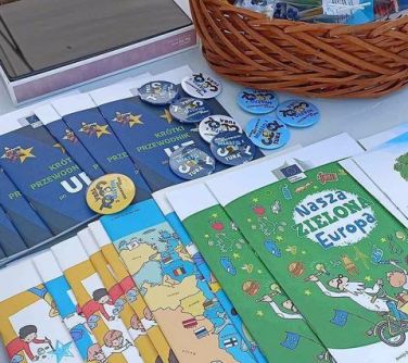 czasopisma i przypinki lezą na stole z prawej strony wiklinowy koszyk wypełniony gadżetami