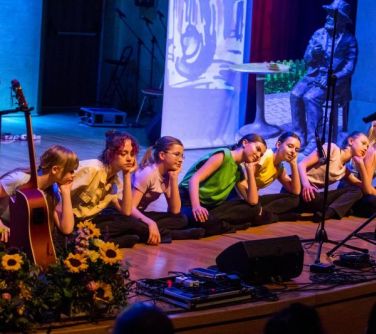 nastolatki siedza po turecku obok siebie na scenia obok stoi gitara