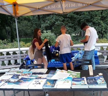 trzy młode osoby przyglądają się granatoym materiałom promocyjnym, rozłożonym na ławkach