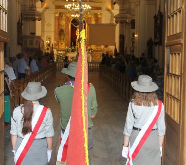 na pierwszym planie harcerski poczet sztandarowy stojący w wejsciu do kościoła, w tle rozświetlony ołtarz