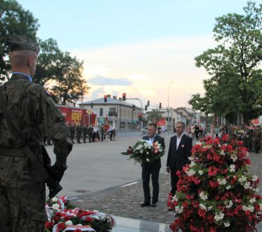 dwóch mężczyzn z wieńcem stoi przy pomniku niepodległości