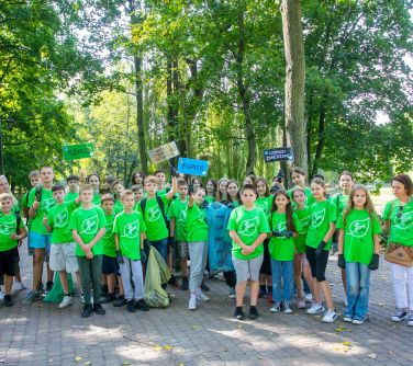 grupa nastolatków wraz z opiekunem w zielonych koszulkach pozują do zdjęcia stoją w alejce parkowej, niektórzy trzymają w...