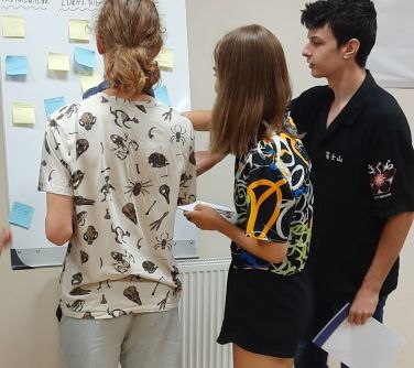 trzy młode osoby naklejają karteczki na tablicę