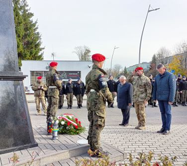 trzech mężczyzn składa hołd pod pomnikiem, przy pominku straż dwóch żołnierzy, w tle żołnierze