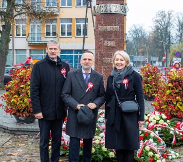 trzy osoby pozują do zdjęcia na tle pomnika niepodległości