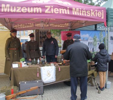 żołnierze po namiotem, przed nimi stoły ze sprzętem wojskowym