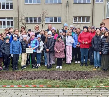 grupa osób pozuje do zdjęcia stojąc na trawniku, w tle budynek szkoly