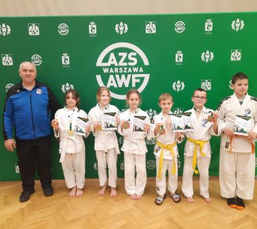 dzieci w kimonach do judo pozują do zdjęcia trzymając w dłoniach dyplomy, po lewej stronie obok dzieci stoi mężczyzna, w...