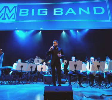 na scenie orkiestra, na przodzie śpiewa mężczyzna, na górze napis MM BigBand