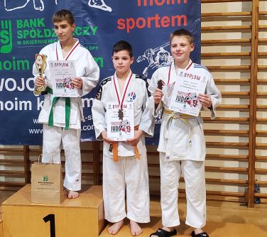 trzech chłopców pozuje do zdjęcia , ubrani są w kimona do judo, w rekach trzymaja dyplomy, na szyi medale