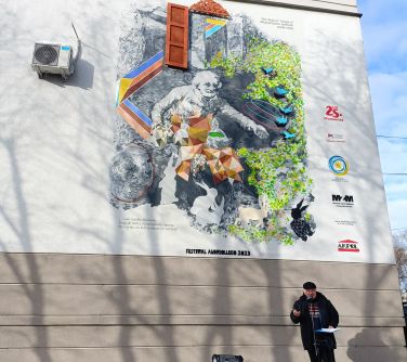 Dwór. Ściana budynku, na niej kolorowy mural, obok mężczyzna