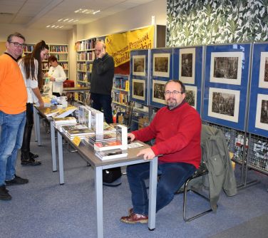 Sala w bibliotece. Na stołach książki, pięć osób naokoło stołów, jeden mężczyzna siedzi na krześle