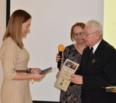 Trzy osoby. Jedna kobieta trzyma mikrofon. Mężczyzna trzyma dyplom