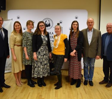 Aula w bibliotece. Na krzeslach siedza osoby. na przodzie kobieta i mężczyzna grają na instrumentach