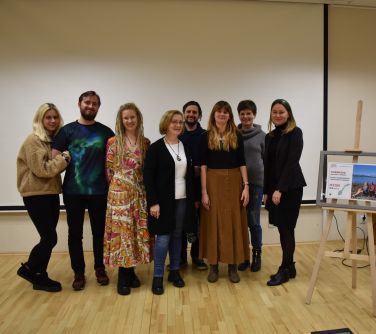 Aula. Osiem osób pozuje do zdjęcia na tle dużego ekranu