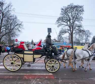 Dwór. Na ulicy przejeżdża karoca ciągnięta przez dwa białe konie. W karocy dwie osoby