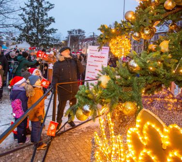 Dwór. Zima. Mężczyzna patrzy na zapaloną choinkę. obok czwórka dzieci. W tle osoby