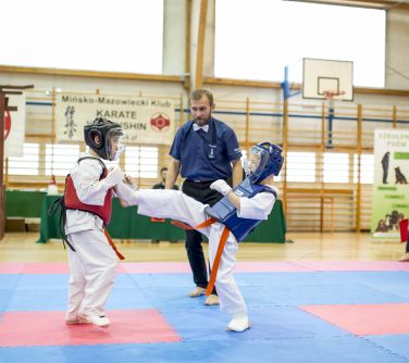 Hala sportowa. dwóch chłopców walczy na macie w kimonach iochraniaczach. Pomiędzy nimi sędzia