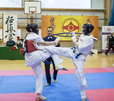 Hala sportowa. Dwóch nastolatków walczy namacie w kimonach i ochraniaczach. Pomiędzy nimi sędzia