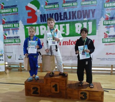 Hala sportowa. Na podium stoi trzech chłopców. Chłopcy trzymają dyplomy w dłoniach, na szyjach medale. Dwóch z nich trzyma...