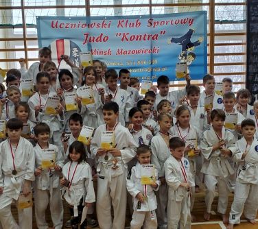 Hala sportowa. Grupa dziei w kimonach pozuje do zdjęcia. Trzymają w dłoniach dyplomy. Na szyjach widnieją medale