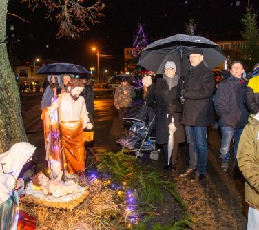 Na dworze, wieczór. Na placu przy szopce stoją zgromadzone osoby