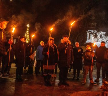 Na dworze wieczór. Osoby stoją nad nie zapalonym ogniskiem z zapalonymi pochodniami