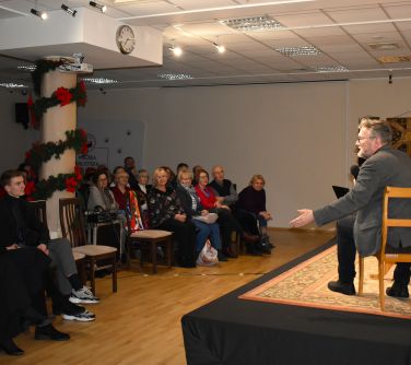 Aula. Po prawej na scenie na krzesłach siedza trzy osoby, Po lewej na krzesłach siedzi widownia