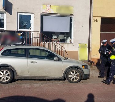 Na dworze w ciągu dnia, na dreptaku dwóch policjantów w mundurach spisują dane stojącego samochodu