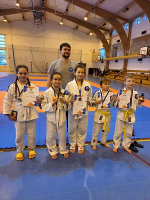Hala sportowa. Pięcioro dzieci i za nimi jeden mężczyzna. Dzieci trzymają dyplomy, na szyjach medale