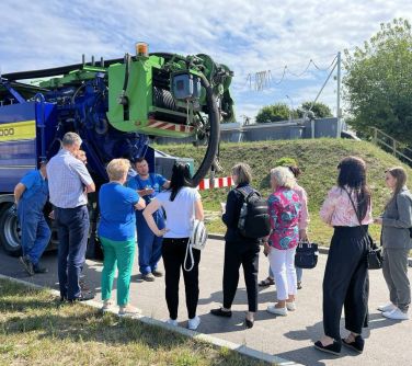 Na dworze. Dziesięć osób stoi na chodniku przed dużym samochodem do wypompowywania wody