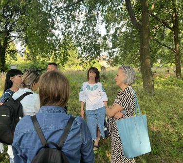 Park. Sześć osób stoi na trawie, drzewa