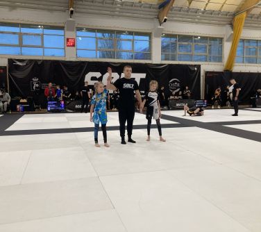 Hala sportowa. Na piankowych matach dwie dziewczynki, pomiędzy nimi sędzia, który podnosi do góry ręke jednej z dziewczynek