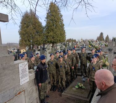 Cmentarz. Pomiędzy grobami grupa młodych żołnierzy w mundurach i niebieskich beretach. Po prawej zarys dwóch mężczyzn