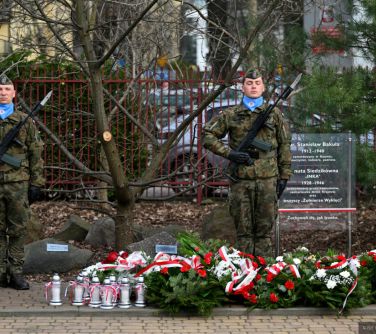 Dwór. Pod tablicą upamiętniająca wiązanki biało-czerwone i znicze. Po jej obu stronach posterunek honorowy żołnierzy