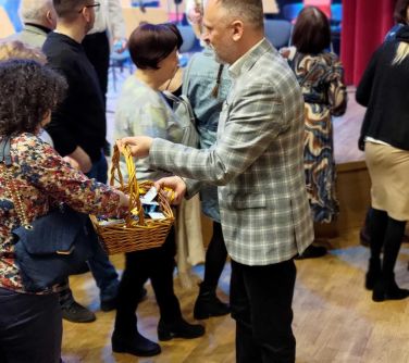 Sala koncertowa. Mężczyzna wręcza upominki z koszyka wiklinowego wychodzącej widowni