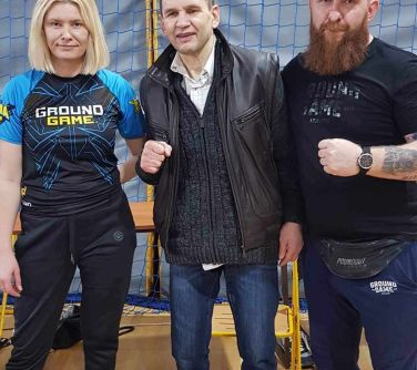 Hala sportowa. Dwóch mężczyzn i kobieta stojąca po lewej stronie pozują do zdjęcia
