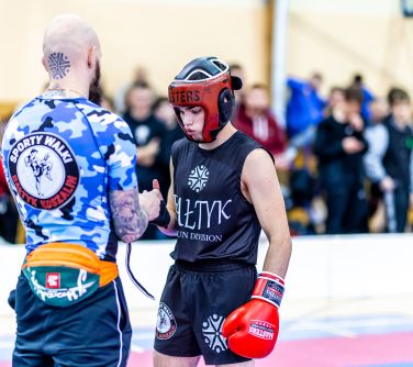 Hala sportowa. Sędzia poprawia zawodnikowi taśmy na dłoni. Na drugiej dłoni rekawica. Na głowie kask. W buzi ochraniacz na...